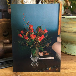 blanc card featuring home scene of blanc arrangement of stunning red roses  in a vase.