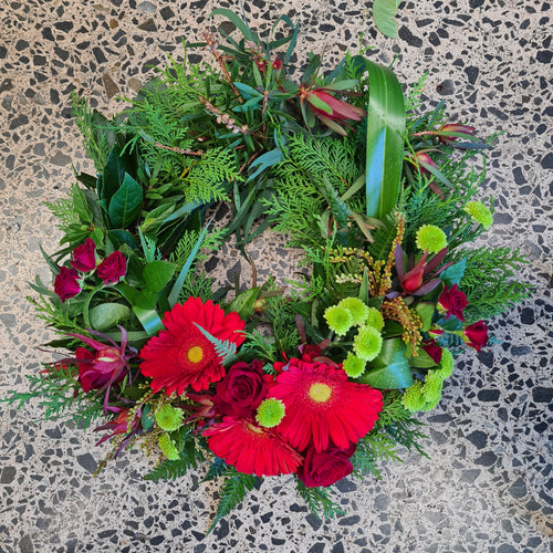 Medium ANZAC wreath by Blanc Flowers in red and green features NZ and Australian native plants with an arc of flowers