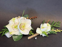 Load image into Gallery viewer, A floral wristlet and matching boutonniere featuring large pale cream hellebore flowers with green leaves, greenery sprigs, small pearl-like beads, and brown twine-wrapped stems, displayed on a dark gray background.
