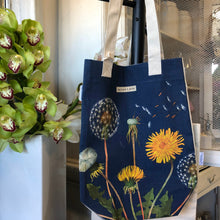 Load image into Gallery viewer, Canvas tote bag, dark blue background with pictures of dandelions in vintage style. By Cavallini  &amp; Co 
